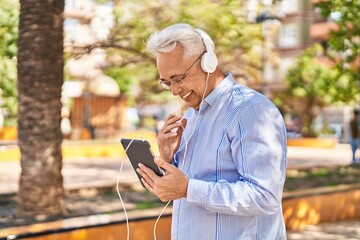 Obraz premium Senior man smiling confident watching video on touchpad at park