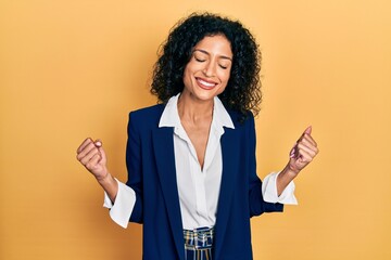 Young latin girl wearing business clothes very happy and excited doing winner gesture with arms...