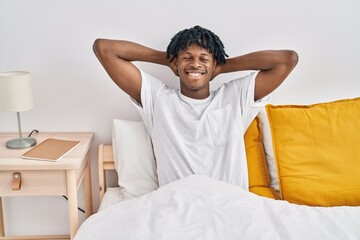 African american man relaxed with hands on head sitting on bed at bedroom