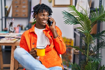 African american man artist drinking coffee talkking on the smartphone at art studio