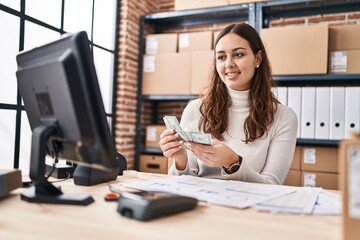 Young beautiful hispanic woman ecommerce business worker counting dollars at office