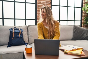 Young blonde woman smiling confident studying using laptop at home