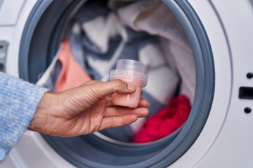 Young woman pouring detergent on washing machine at laundry room