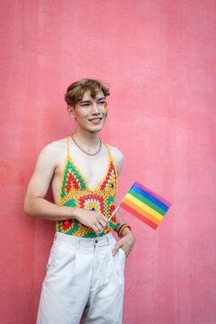 Handsome gay man with pride, holding LGBT Rainbow flag against pink background.