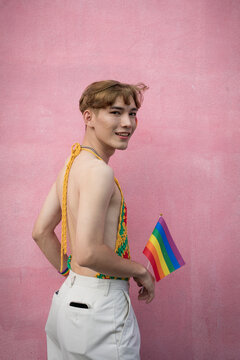 Handsome gay man with pride, holding LGBT Rainbow flag against pink background.