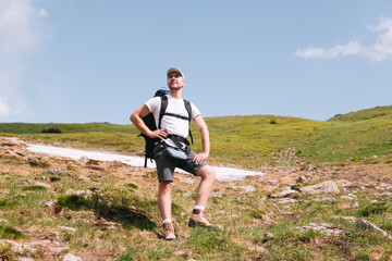 A bearded traveler with a backpack on the top of a mountain. A tourist with a backpack stands against the background of a mountain