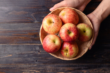 Red apple fruit in basket with hand on wooden background, Table top view