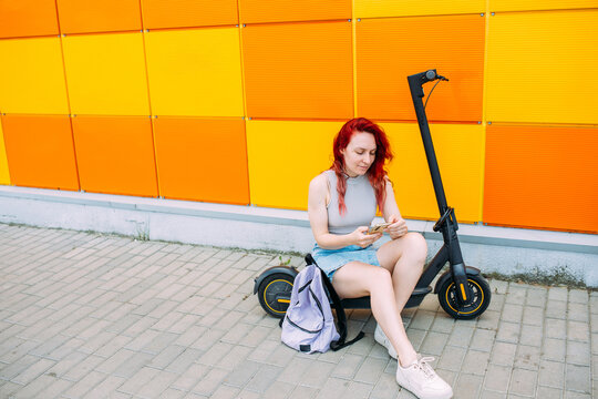 Woman uses a smartphone and an electric scooter in the summer in the city