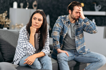 A quarrel in the relationship of a caucasian couple, the spouses quarreled over disagreements, they sit on a sofa in the living room, they are offended by each other, they look in different directions