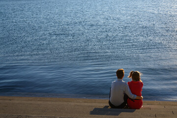 Young couple sitting together by the water in  evening sunlight, copyspace