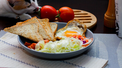 Breakfast, fried eggs, fried sausage, vegetable salad and toast on a brown wooden table with coffee.
