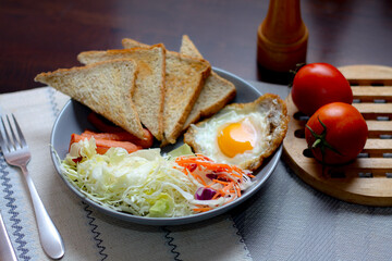Breakfast, fried eggs, fried sausage, vegetable salad and toast on a brown wooden table with coffee.