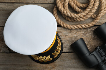 Peaked cap, rope and binoculars on wooden background, flat lay