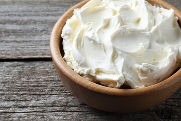Bowl of tasty cream cheese on wooden table, closeup