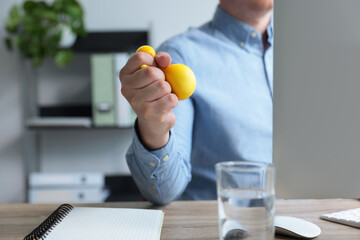 Man squeezing antistress ball while working with computer in office, closeup