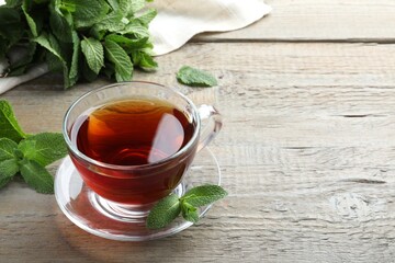 Cup of hot aromatic tea with mint on wooden table. Space for text