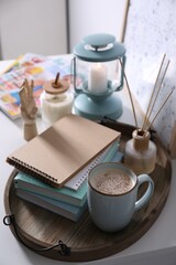 Wooden tray with books, air reed freshener and cup of coffee on white table indoors