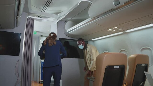 A man helping a passenger woman to put luggage cabin compartment. People wearing face masks on an airplane. travel under Covid-19, New normal, Illness Prevention concept.