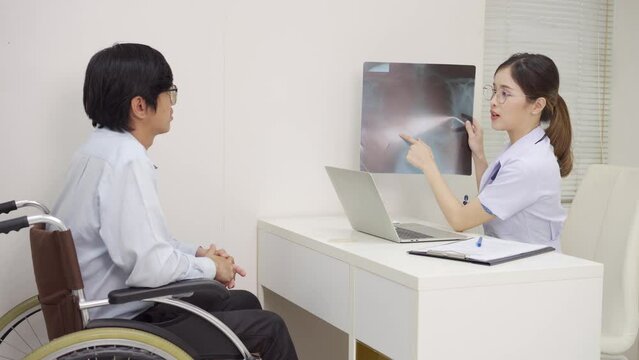 Asian female doctor looking x-ray flim with a patient male in a wheelchair at the hospital.