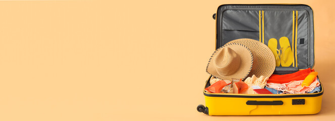 Open suitcase with clothes and beach accessories on beige background with space for text