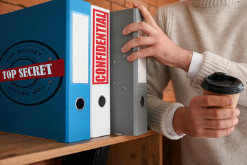 Young man near folders with top secret documents in office