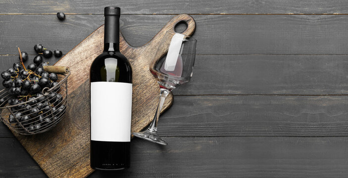 Tasty red wine in bottle with fresh grapes and glass on dark wooden background with space for text
