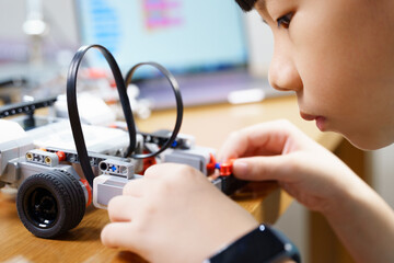 Close up of Asian student child's hands and face assembling and testing touch sensor of vehicle robot, solving engineering problem on table. STEM education and 21st century learning skills concept