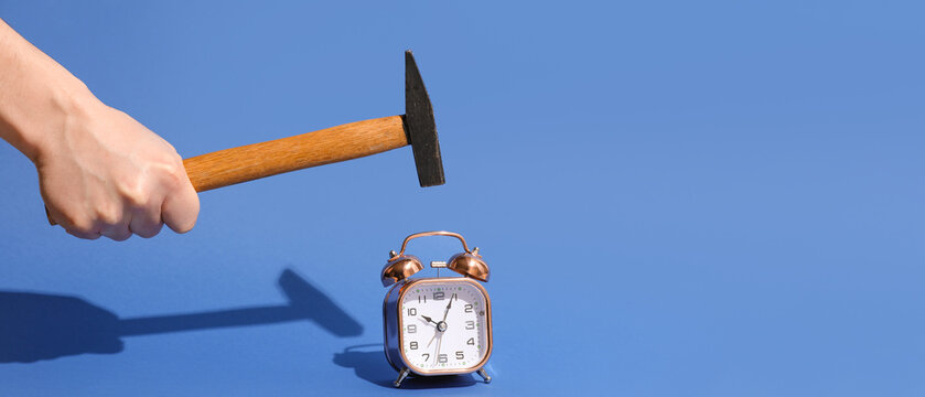 Hand with hammer and alarm clock on blue background