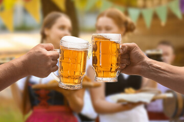 Men clinking mugs with beer during celebration of Octoberfest outdoors