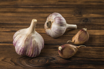 Two cloves of garlic and two heads of garlic on a wooden table.