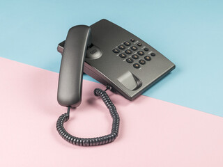 Gray push-button phone with the handset off on a pink and blue background.