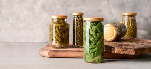 Jars with different canned vegetables on grey background