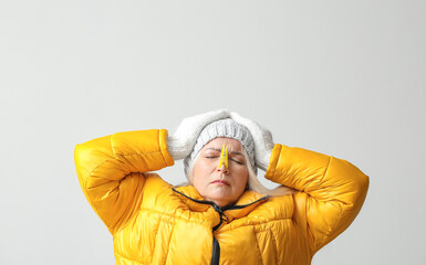 Ill mature woman with clothespin on light background. Stuffy nose concept