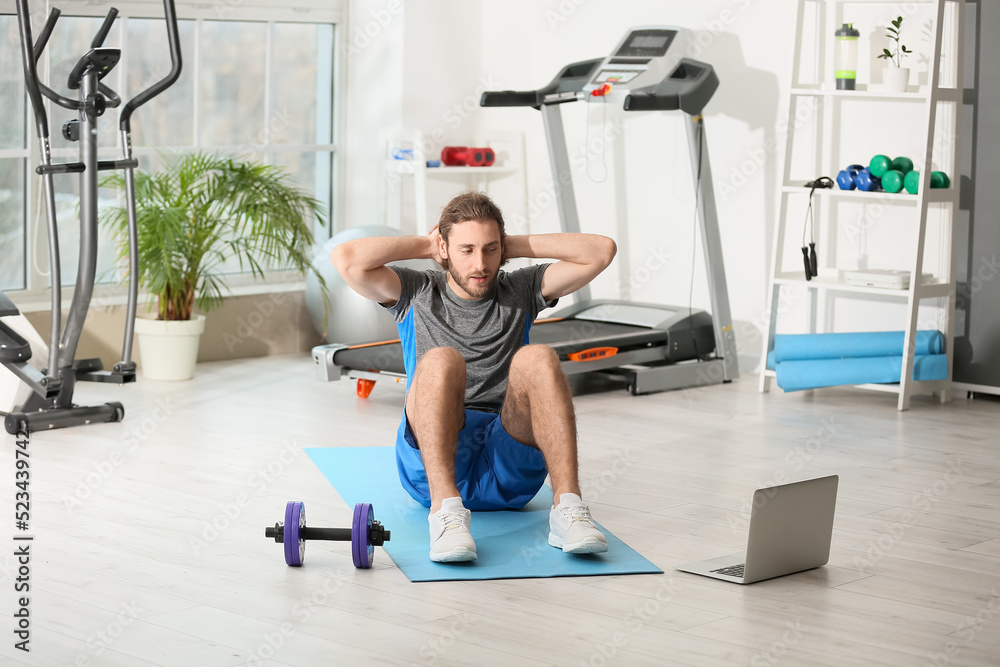 Poster Sporty young man with laptop training in gym