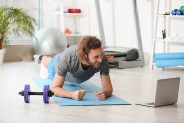 Sporty young man with laptop training in gym