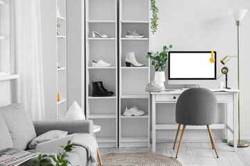 Shelf units with different shoes and workplace with modern computer near white wall