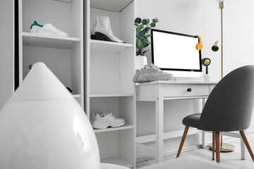 Shelf units with different stylish shoes and workplace with modern computer near white wall