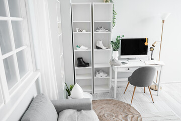 Shelf units with different shoes and modern workplace near white wall in light room interior