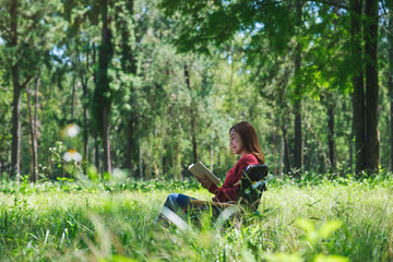 Fototapeta premium Portrait of a beautiful young asian woman reading a book while sitting on a camping chair in the park