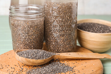 Glasses of water with chia seeds, board and spoon on color wooden background, closeup