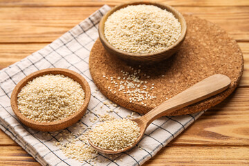 Bowls and spoon with sesame seeds on wooden background, closeup