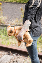 a young caucasian girl with glasses and tattoos smiles, a brown teddy bear 