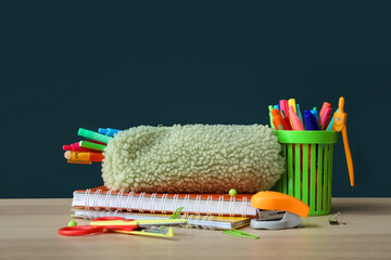 Pencil case with school stationery and pen cup on table against dark background
