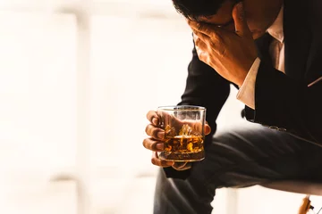 Poster Alcoholism, depressed asian young man sleep on table while drinking alcoholic beverage, holding glass of whiskey alone at night. Treatment of alcohol addiction, suffer abuse problem alcoholism concept © makibestphoto