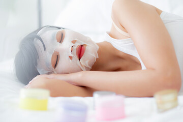Obraz na płótnie Canvas Beautiful young asian woman with sheet facial mask on bed at bedroom, beauty girl lying applying cosmetic and makeup with skin care face for wrinkle at home, one person, skincare treatment and health.