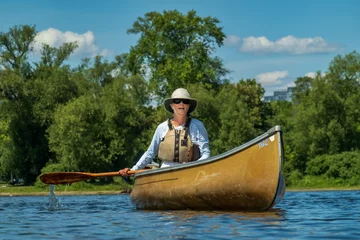 Foto op Canvas A woman of retirement age solo paddles a canoe around the Toronto Islands wearing sun safe clothing in midday sun.. © Michael Connor Photo