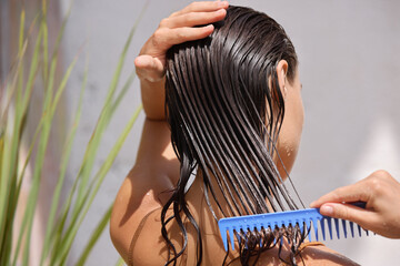 Young Female Model Putting Refreshing Mask On Long Wet Hair With Wooden Comb. Closeup Of Beautiful...