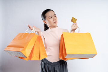 Asian woman guilty worried nervous holding more shopping bags and credit card isolated over...