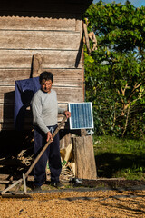 Latino man working on drying coffee, in front of his cabin with a solar panel