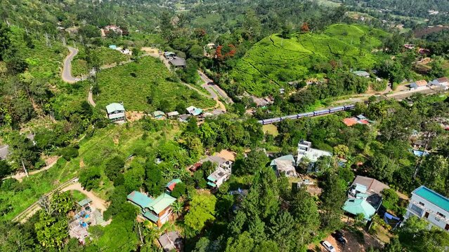 Aerial Panning Shot Of Train Moving On Tracks Amidst Green Landscape, Drone Flying Over Trees During Sunny Day - Ella, Sri Lanka